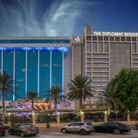 The Diplomat Radisson Blu Hotel Residence & Spa Manama Exterior photo The photo features two large buildings, likely hotels or residences. On the left, there’s a blue glass facade with illuminated signage, possibly indicating a hotel or establishment, with trees in front. On the right, there’s a building labeled "The D